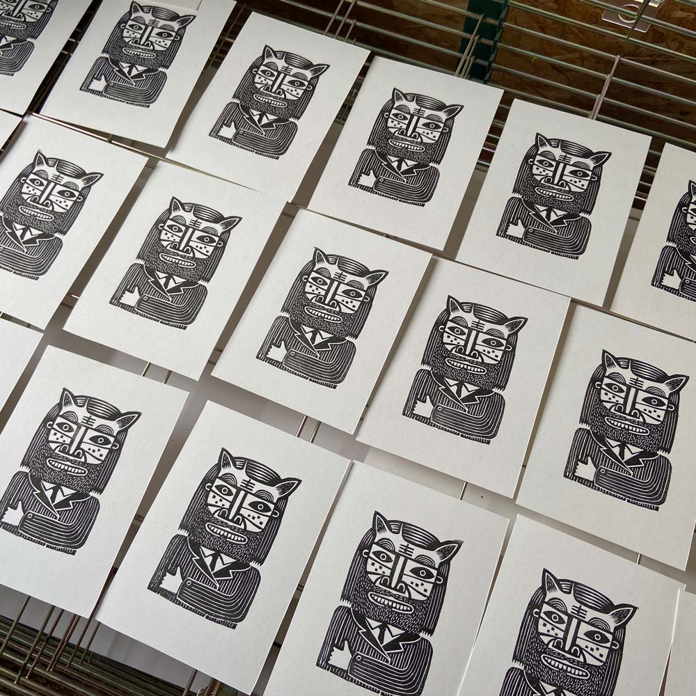 Black and white linocut image of a man cat wearing a pinstripe suit and holding up a thumb